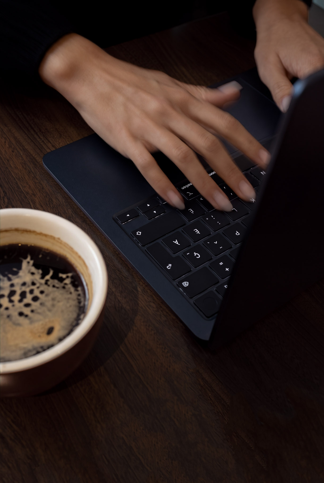 Mains sur un clavier à côté d'un café, sur une table en bois
